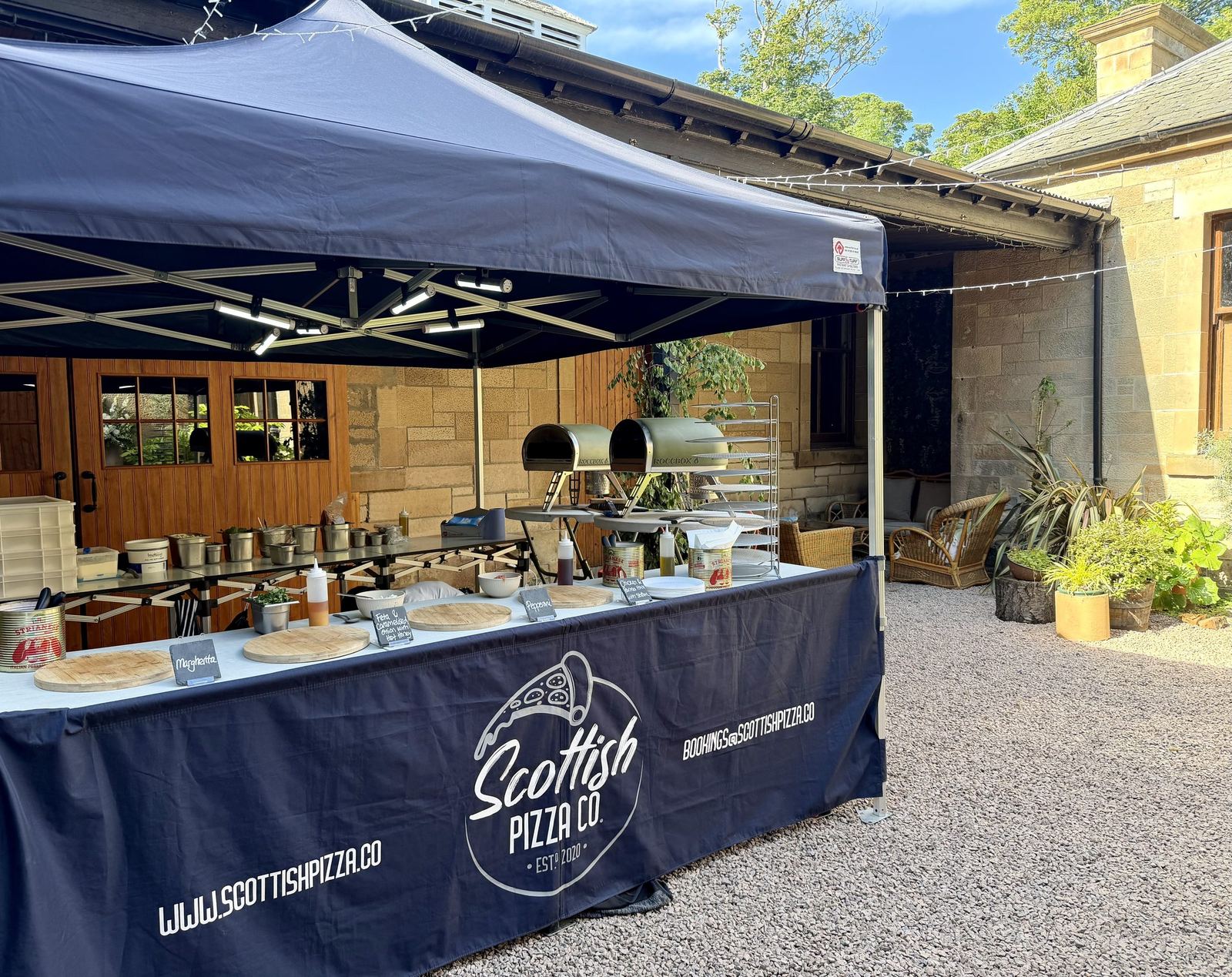 Scottish Pizza Co pizza pop-up station set up in a stone courtyard, branded navy counter with pizzas ready to serve