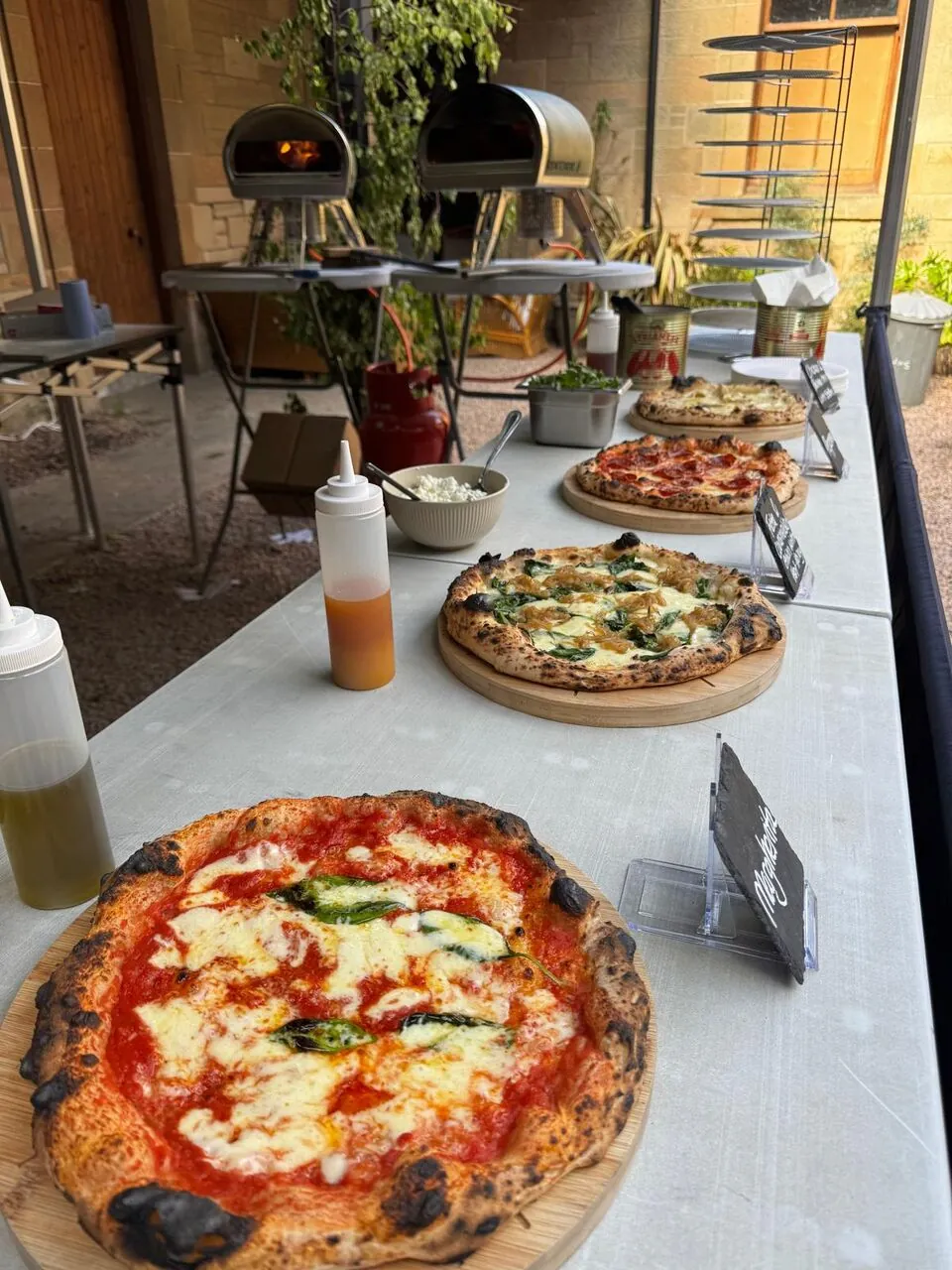 Margherita and other fresh pizzas on wooden boards along the serving table at a Scottish Pizza Co courtyard pop-up