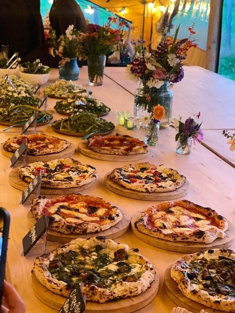 Pizzas and salads laid out along a long rustic table