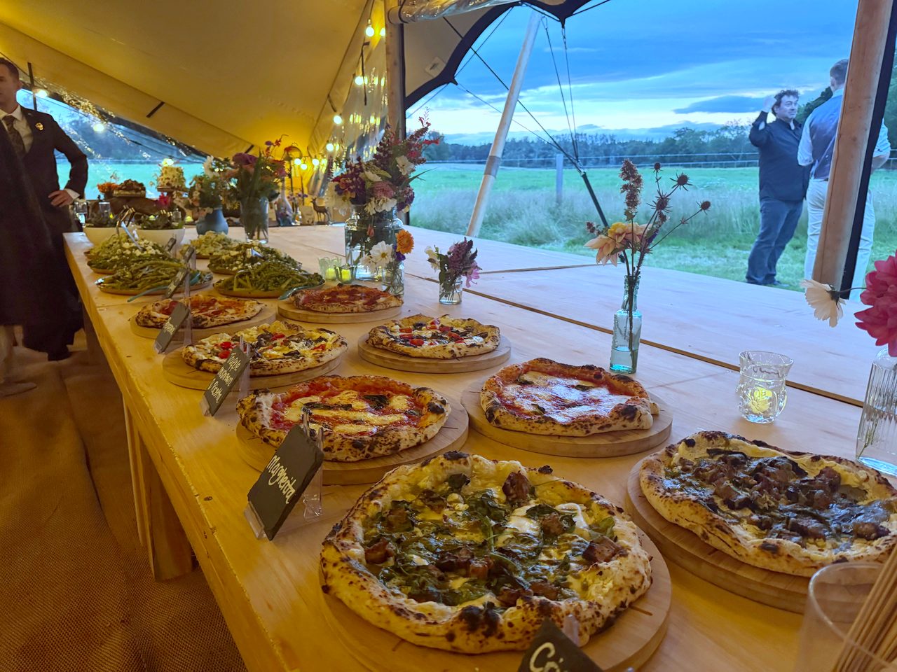 Long table of pizzas in a marquee at sunset at a wedding