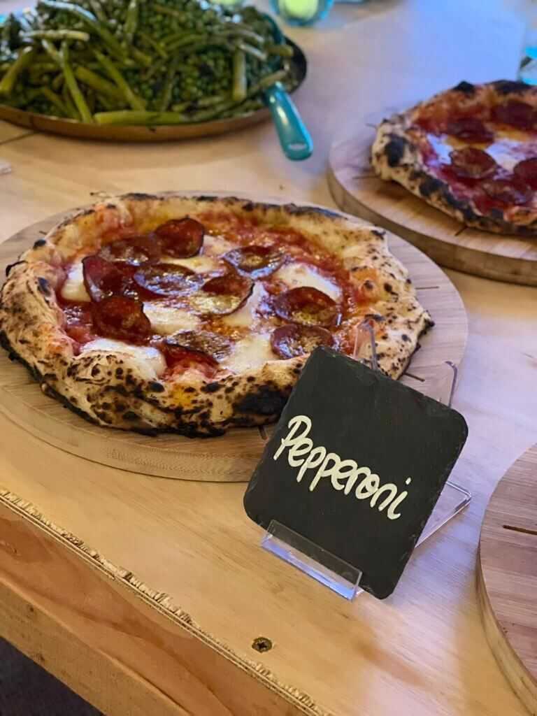 Pepperoni pizza on a wooden board with a chalkboard label