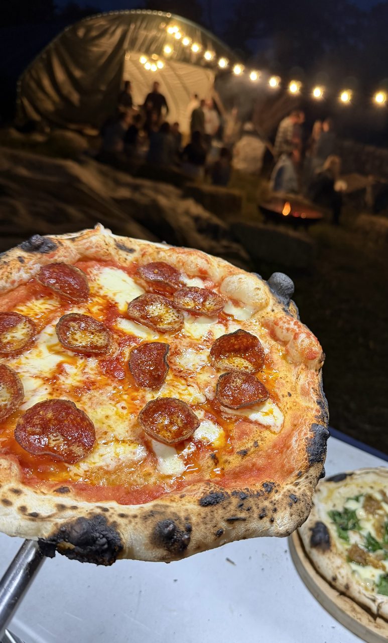 Freshly cooked pepperoni pizza held up at an evening garden party with festoon lights