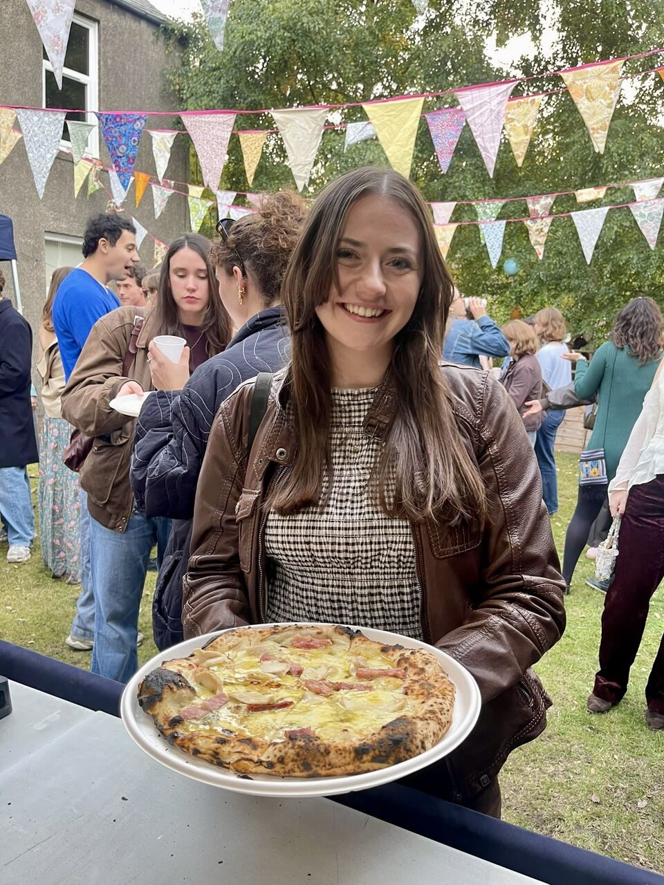 Smiling guest holding a pizza at a garden party with bunting