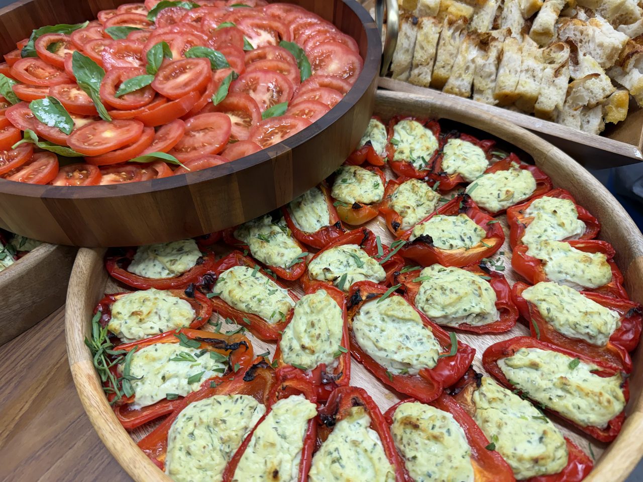 Wooden sharing bowls of stuffed peppers and tomato salad laid out for wedding guests